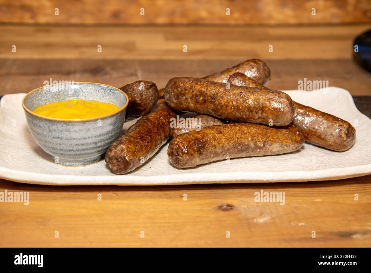 A plate of delicious sausages and a little pot of mustard on a wooden kitchen work top Stock Photo