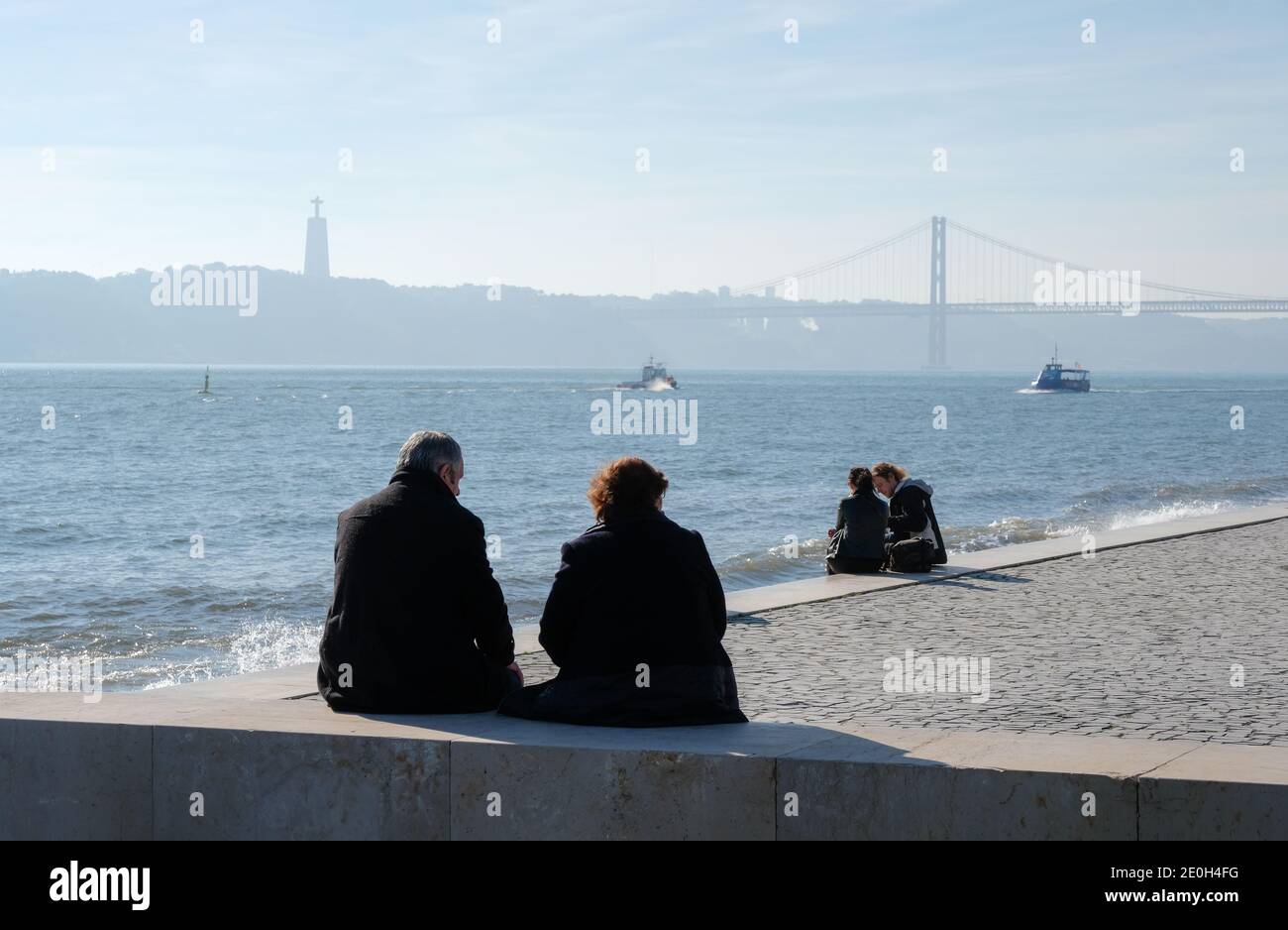 Middle-aged couple sitting the river Tagus near the 25 de Abril bridge (April 25 bridge) and the Cristo Rei - Statue of Jesus Christ. Lisbon, Portugal Stock Photo