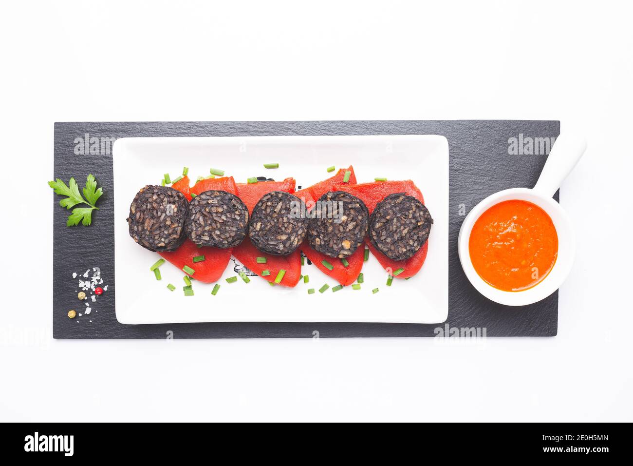 Slices of Spanish black pudding on piquillo peppers in white plate on white background. Spanish tapas. Stock Photo