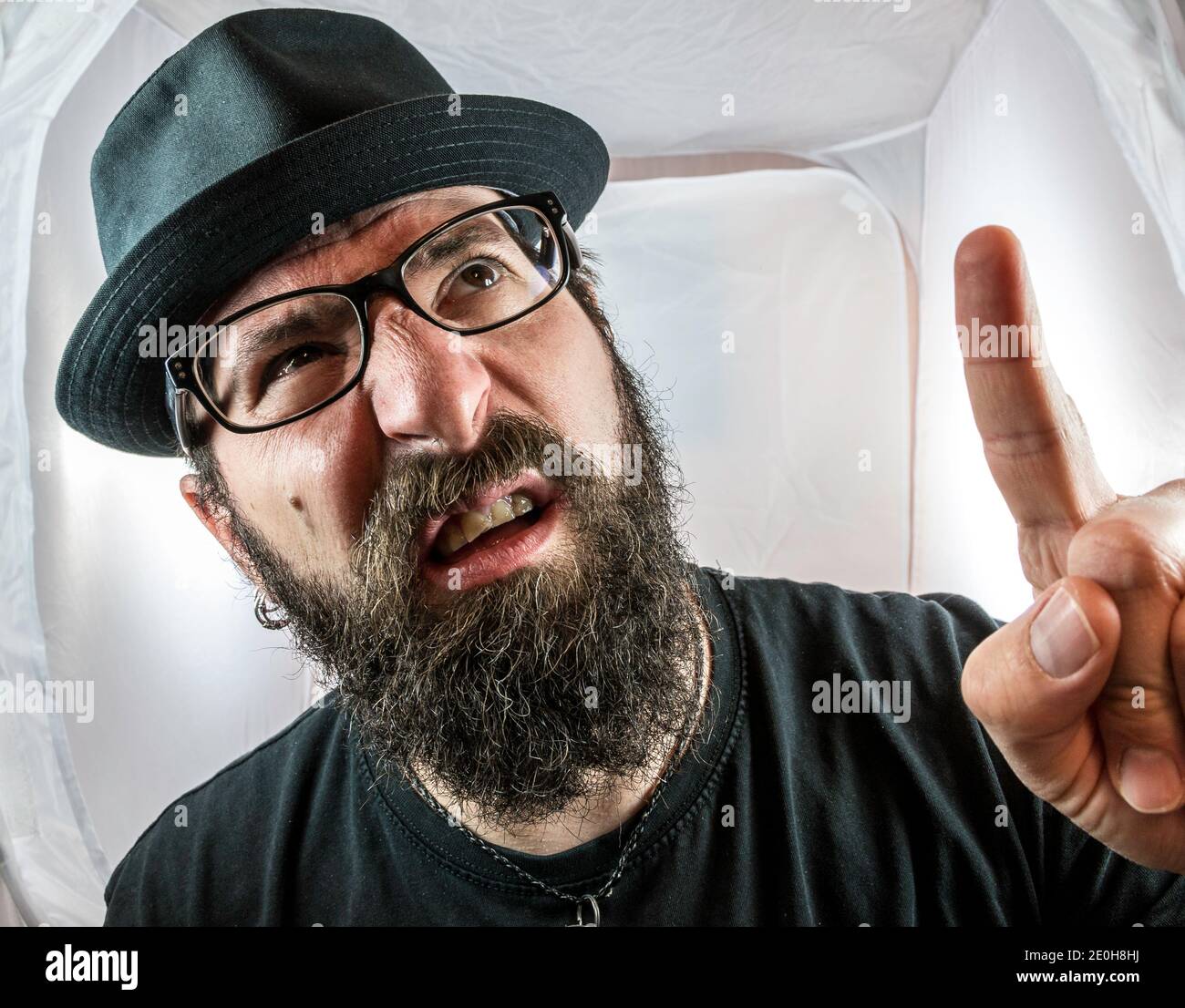 A bearded man with black glasses and hat showing finger and looking questioning Stock Photo
