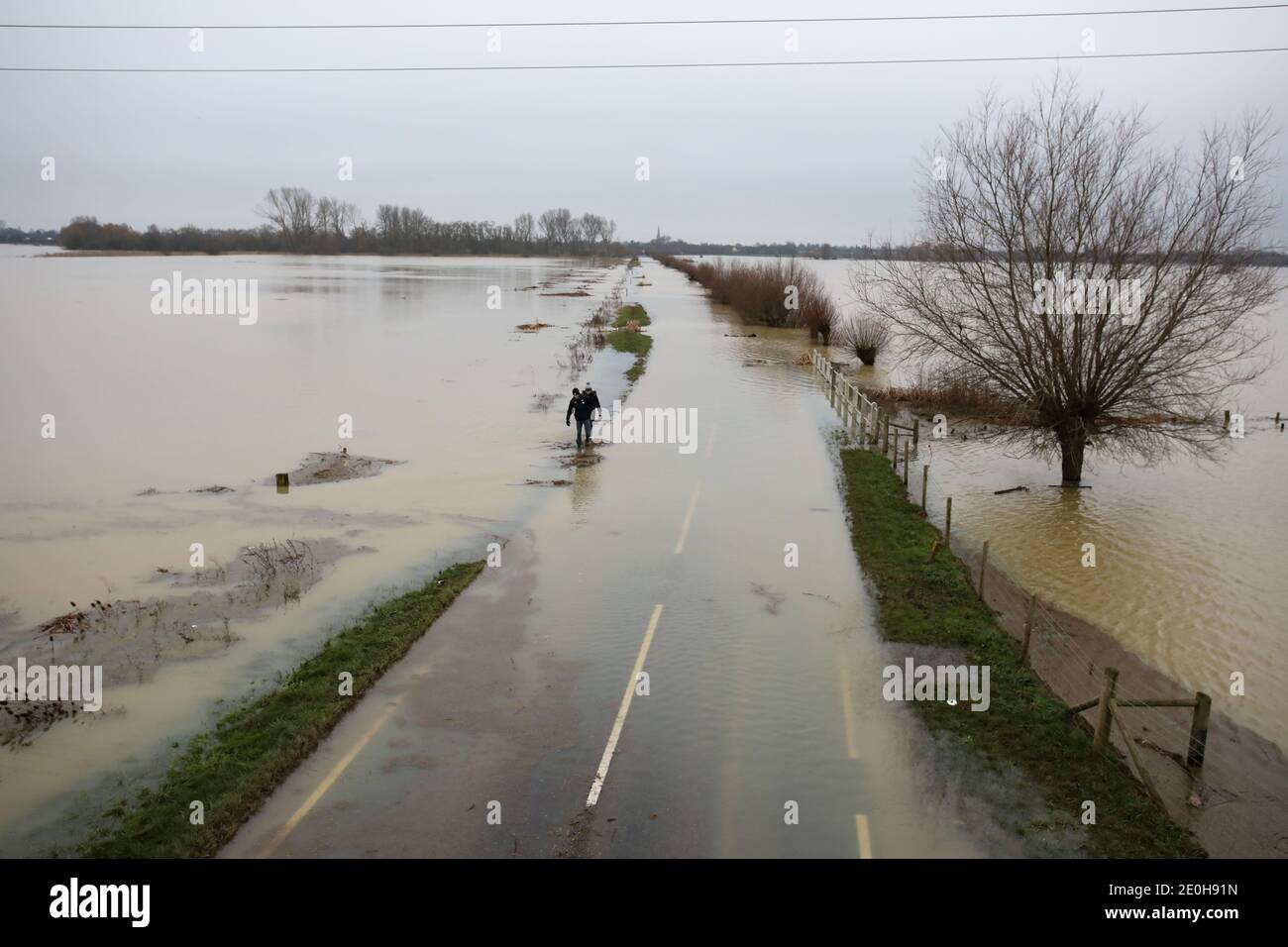Whittlesey, UK. 29th Dec, 2020. People manage to walk along high parts of the road verge as floodwater has forced the closure of this road near Whittlesey, Cambridgeshire, after the River Nene burst its banks last week, and excess water is now sitting on the flood plains. Credit: Paul Marriott/Alamy Live News Stock Photo