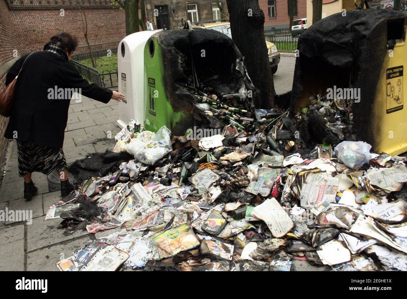 Cracow. Krakow. Poland.  Burnt garbage lying by vandalised selective waste collection containers. Woman dropping garbage. Stock Photo