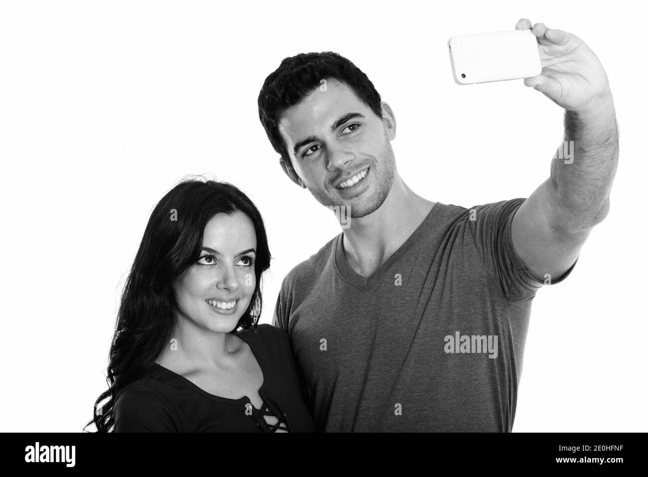 Studio shot of young happy couple smiling while taking selfie picture with mobile phone together with man holding phone Stock Photo