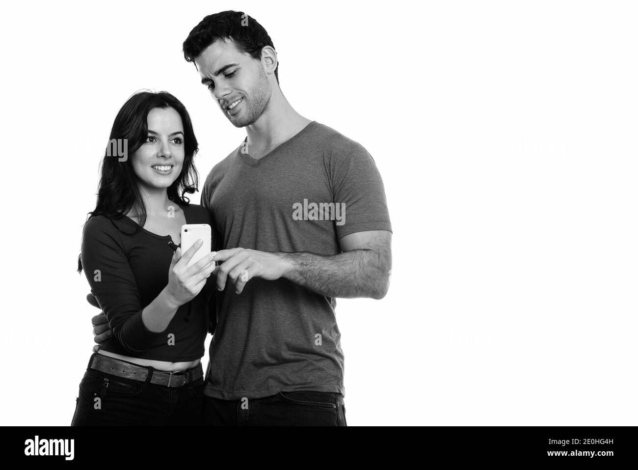 Studio shot of young happy couple smiling with man using mobile phone and woman thinking Stock Photo