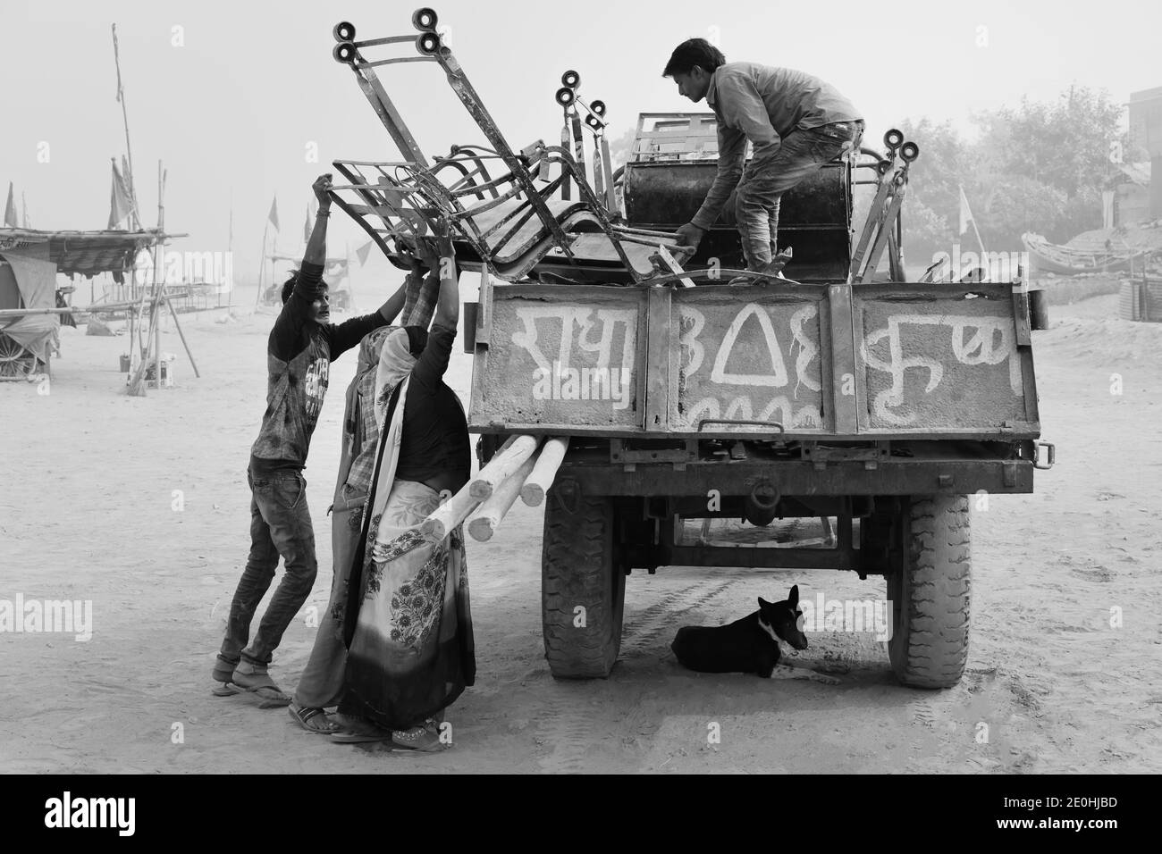 Two omen and man load dismantled chairs of big wheel onto waiting truck on hot summer day alongside river Yamuna in Vrindavan, Uttar Pradesh, India. Stock Photo
