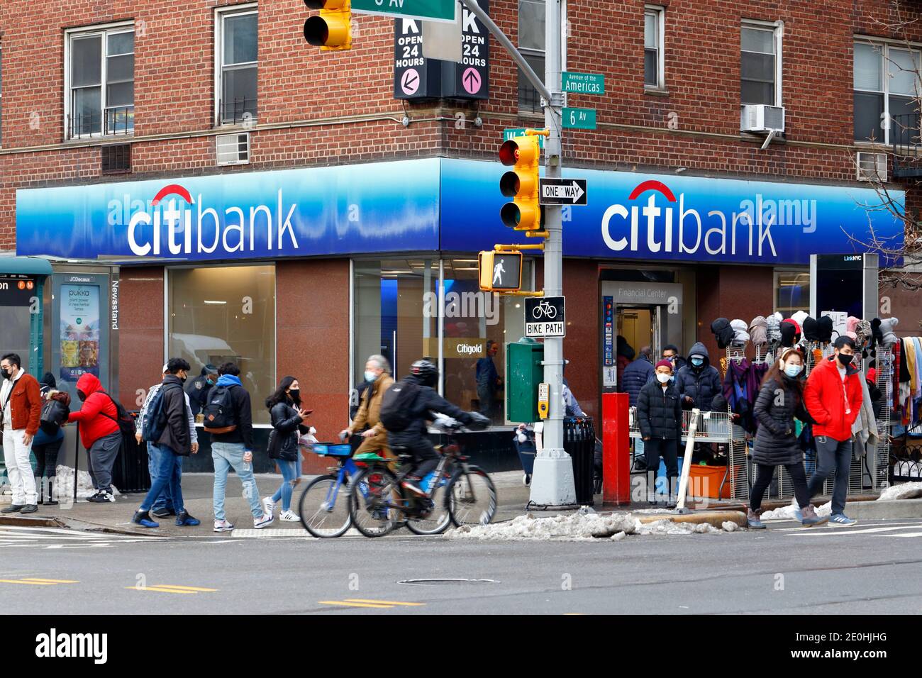 People wearing masks, bicyclists, pedestrians, snow, street vendors, and Citibank on the corner of 6th Ave and W 23rd St in New York, NY. Dec 2020 Stock Photo