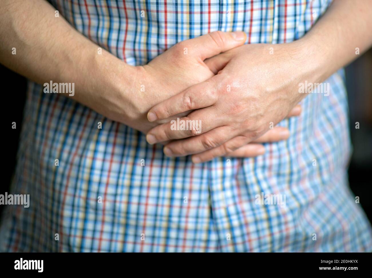 Man in a shirt holding hands on his stomach, closeup on the hands Stock Photo