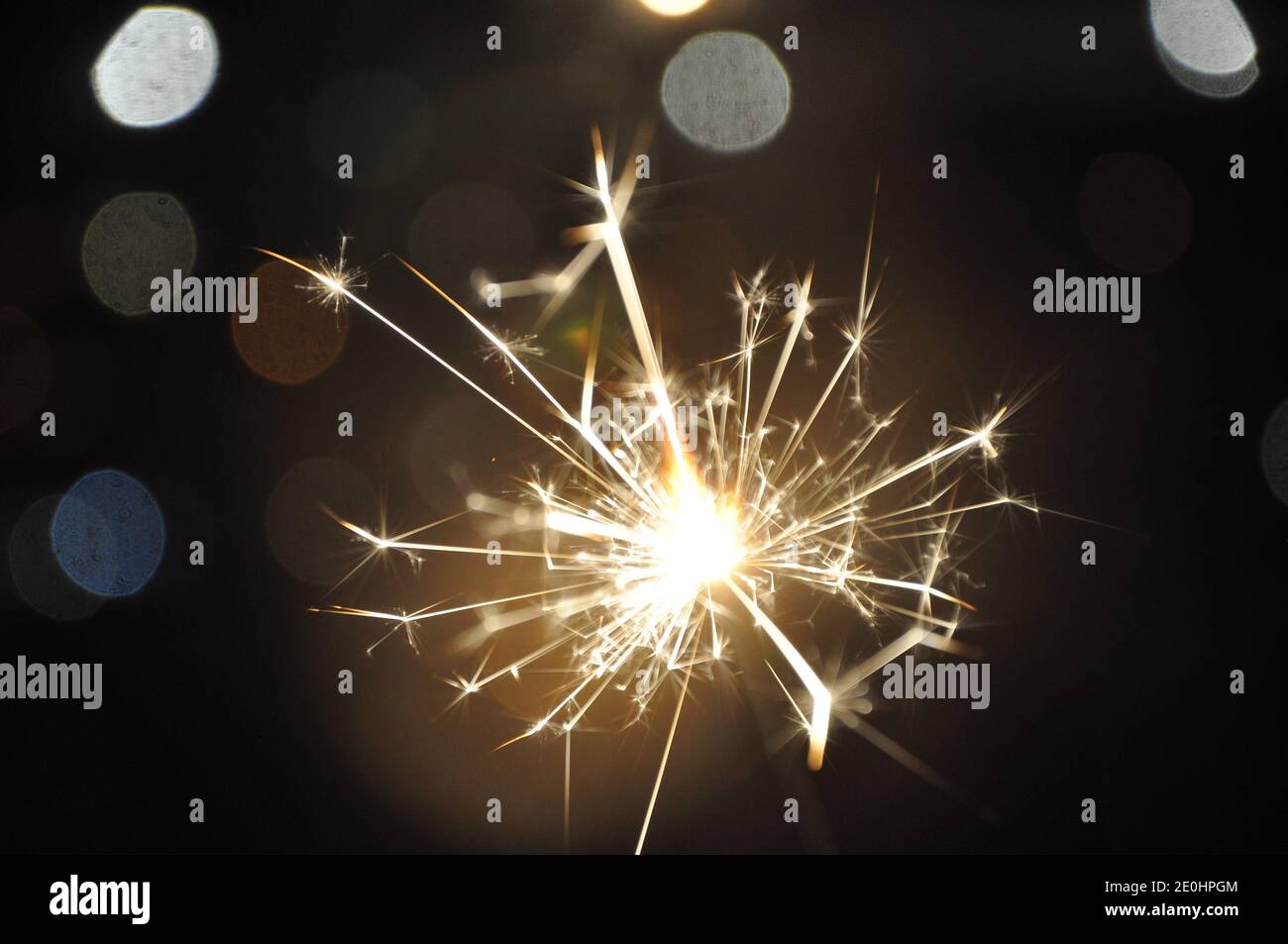 Burning sparkler in the night with bokeh. Glittering burning sparkler with bokeh light background. Stock Photo