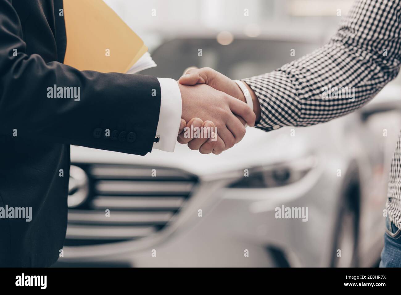 Close up cropped shot of a man shaking hands with professional car dealer at automobile dealership. Salesman shaking hands with his client after selli Stock Photo
