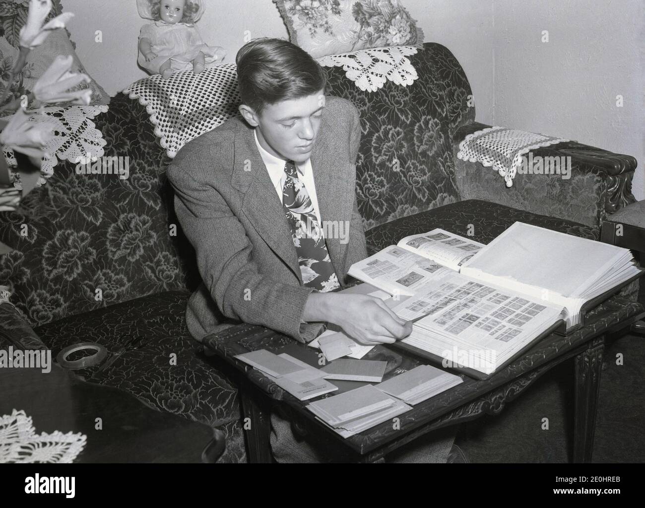 1948, historical, a smartly dressed young man in a jacket and tie sitting on a sofa looking through his stamp collection, USA. The popular hobby or pasttime of collecting stamps is one of the areas that makes up the wider subject of 'philately', which is the more serious, study of stamps, although a philatelist may, but does not have to, collect stamps. Postage stamps are collected for their possible historical value and their wide and varied subject matter. Stock Photo