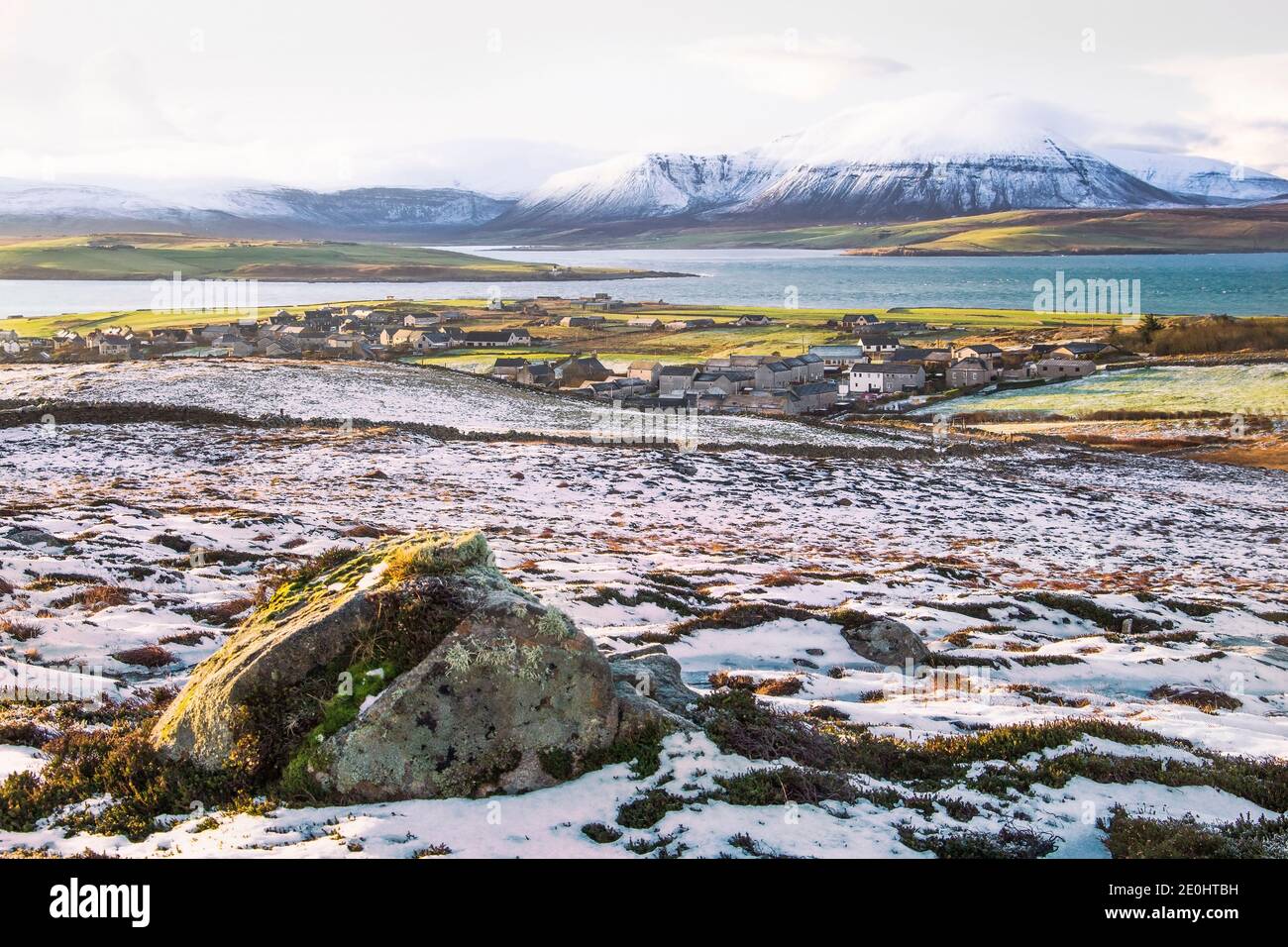 Winter view of scottish islands on Orkney with town of Stromness below the hill and big stone in foreground Stock Photo