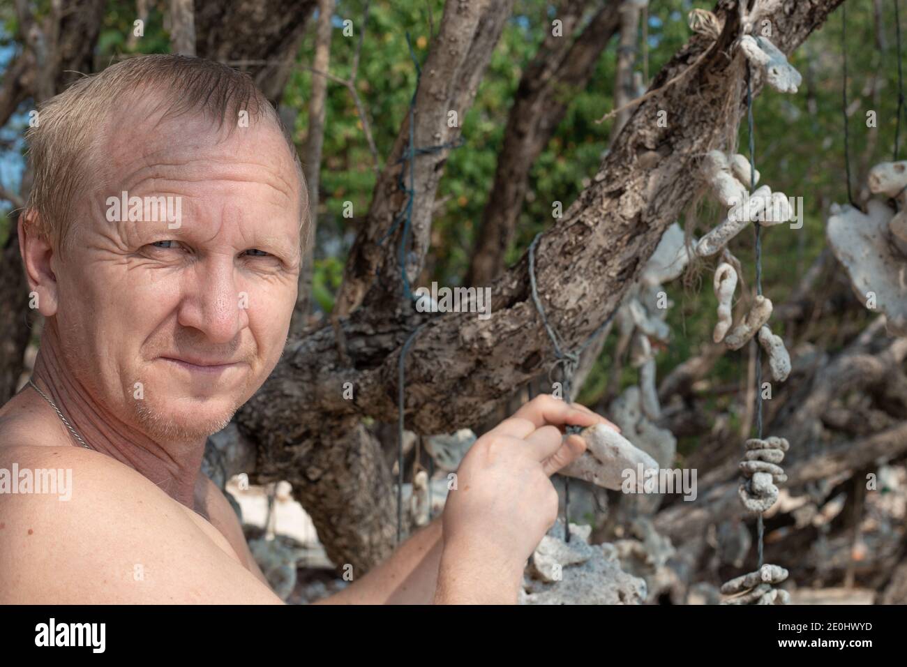 adult Caucasian man close-up on a tropical island tying corals to a tree. Make a wish. Holidays in Asia Stock Photo