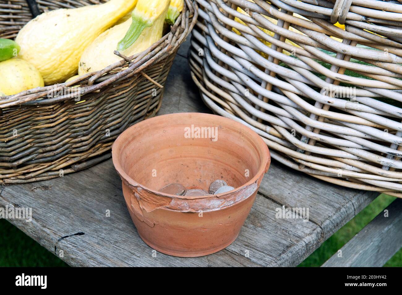 Chipped Terracotta flower pot with takings inside money from the sale of vegetables in between two wicker baskets Stock Photo