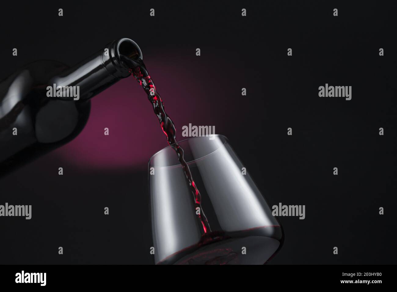Bottle of red wine poured into the wine glass, on black and red background. Stock Photo