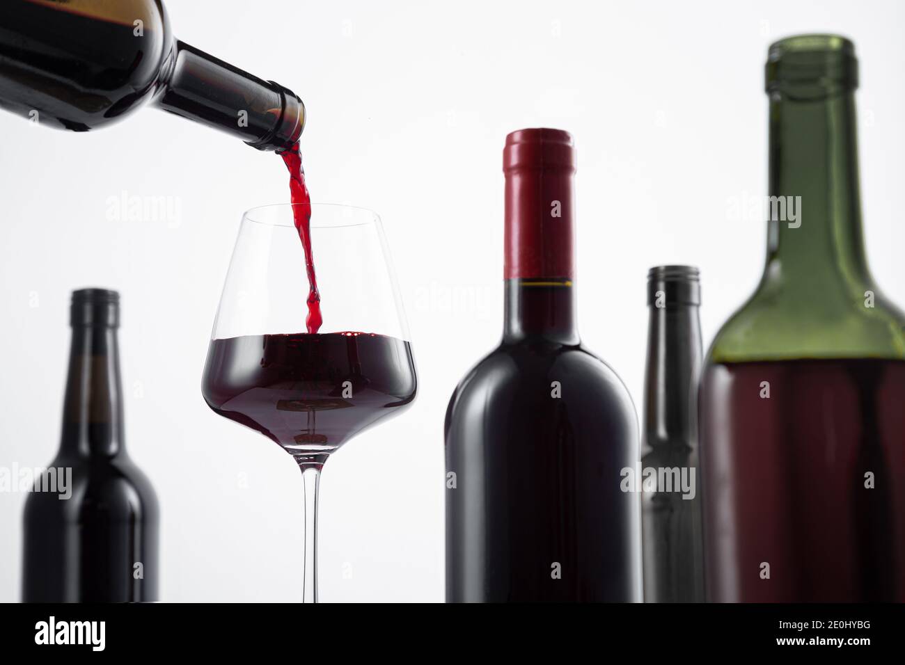 Bottle of red wine poured into the wine glass, and variety of wine bottles with selective focus on  white background. Stock Photo