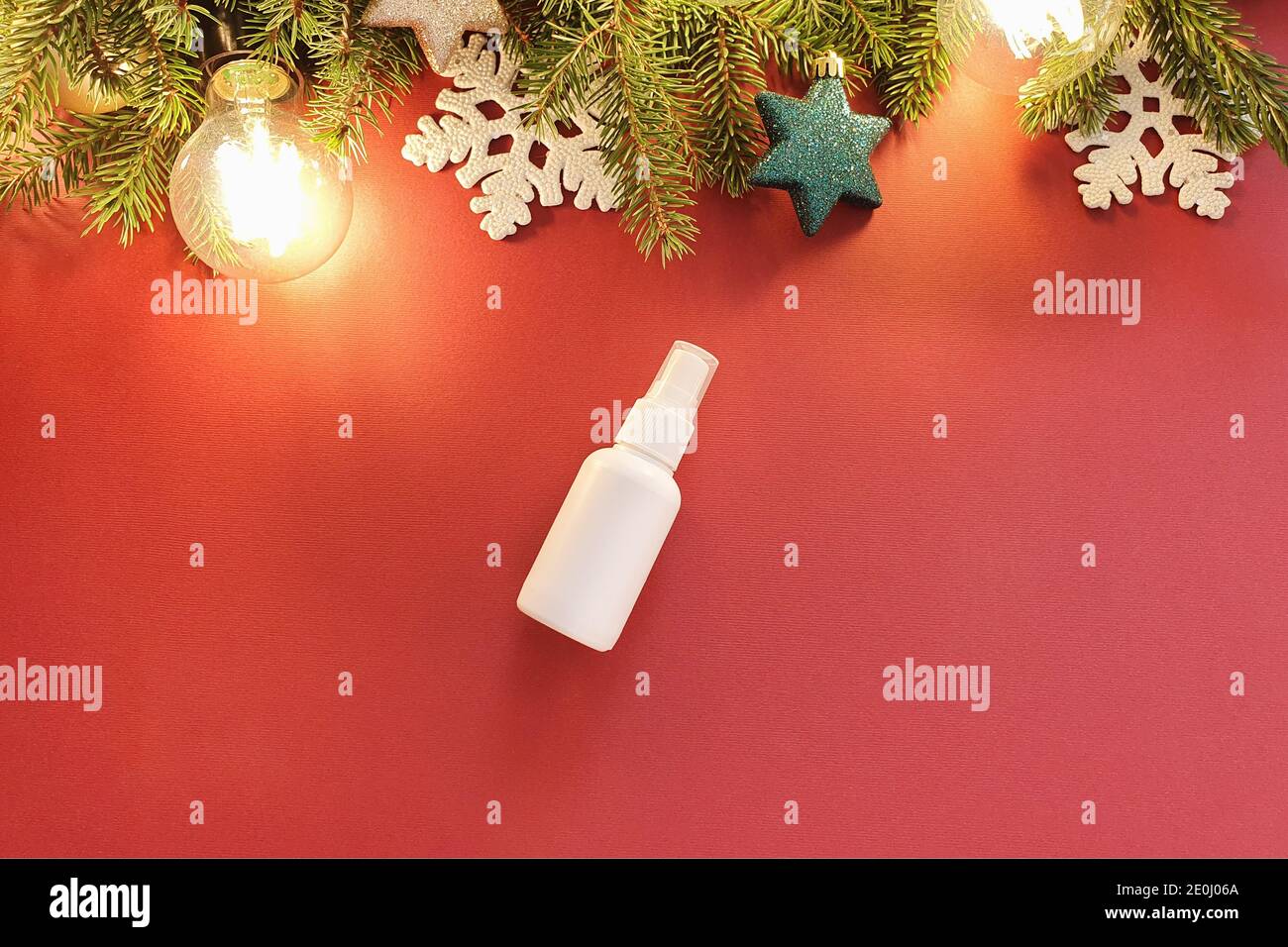 Mock-up of white plastic spray bottle, Christmas fir tree and Christmas decorations on a red background. Top view, flat lay style. Stock Photo