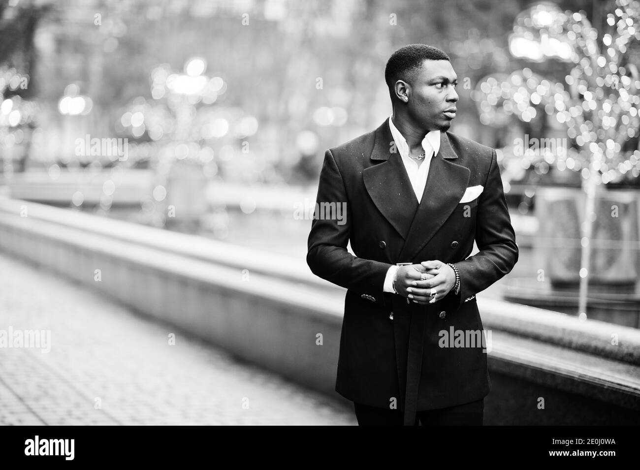 Portrait of young and handsome african american businessman in suit walking on cemter of city with garlands. Stock Photo