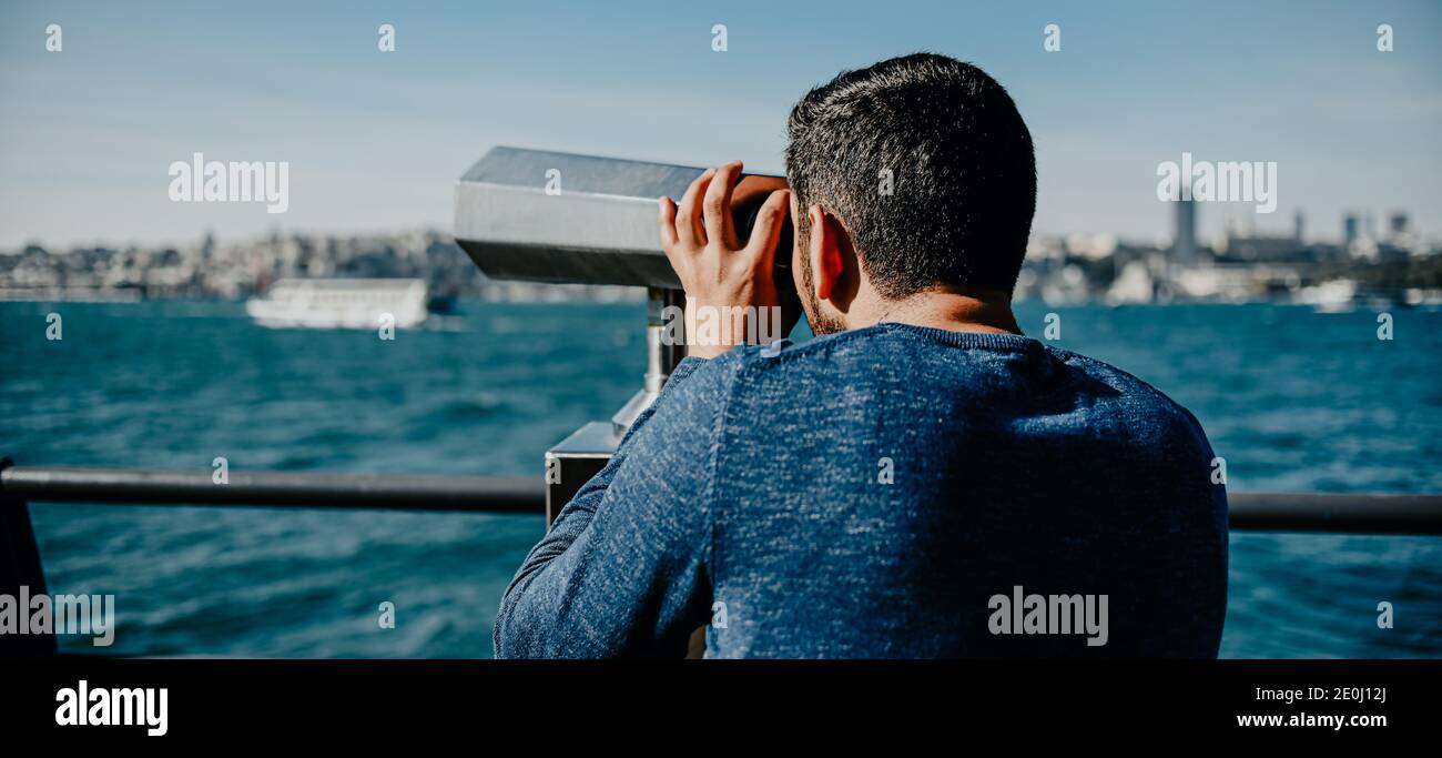 Turkish tanned guy looks at the panorama of the city of Istanbul with binoculars with a coin receiver on the observation deck promenade banner Stock Photo