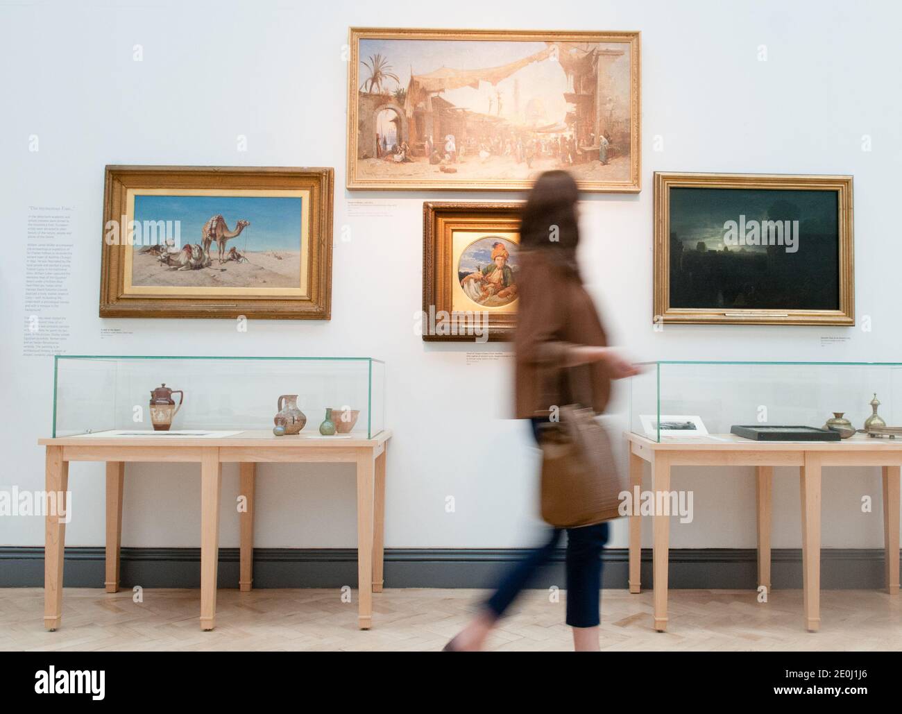 White young woman alone walking past oil paintings in an art gallery, she is blurred showing motion as she turns her head to look at the artworks Stock Photo