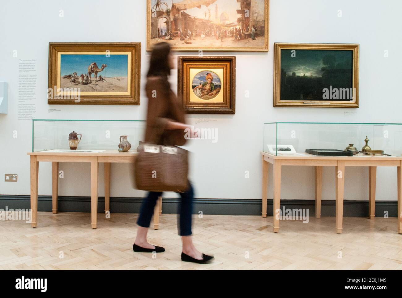 White young woman alone walking past oil paintings in an art gallery, she is blurred showing motion as she turns her head to look at the artworks Stock Photo
