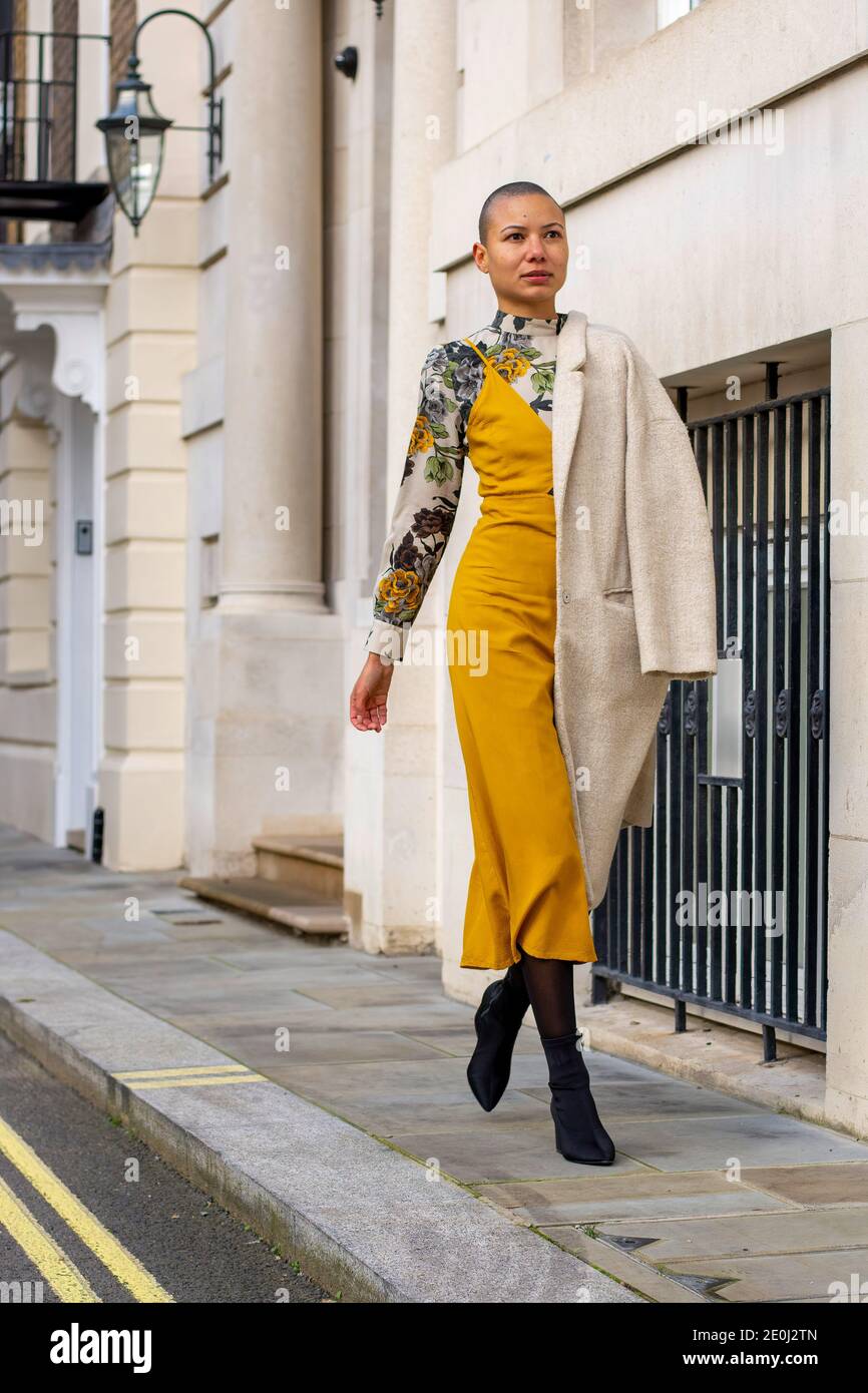 A model wearing a Milk & Roses slip midi dress worn over Zara floral, high  neck midi dress, styled with a cream long line coat and black tights &  boots, walking on