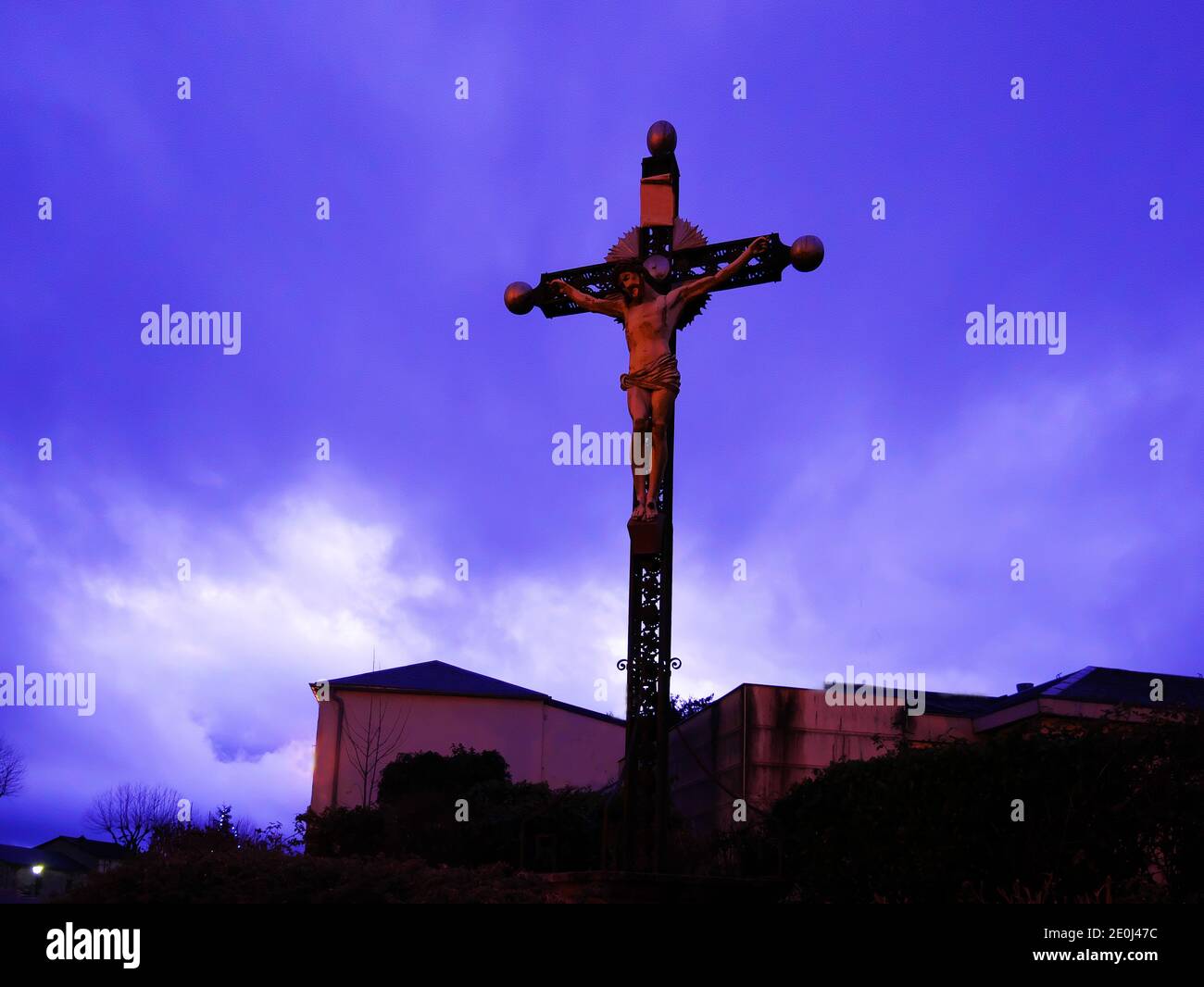 Religious metal cross with the statue of Jesus Christ, photo taken in the evening under a cloudy sky. Stock Photo