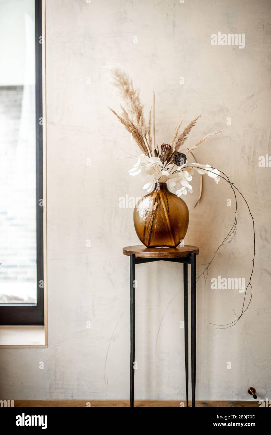 Composition of dried flowers and herbs in a glass vase on a beige wall background. Bouquet of pampas, grass, Cortaderia, nelumbo, banksia, Proteaceae, Eucalyptus, Stabilized plants Stock Photo