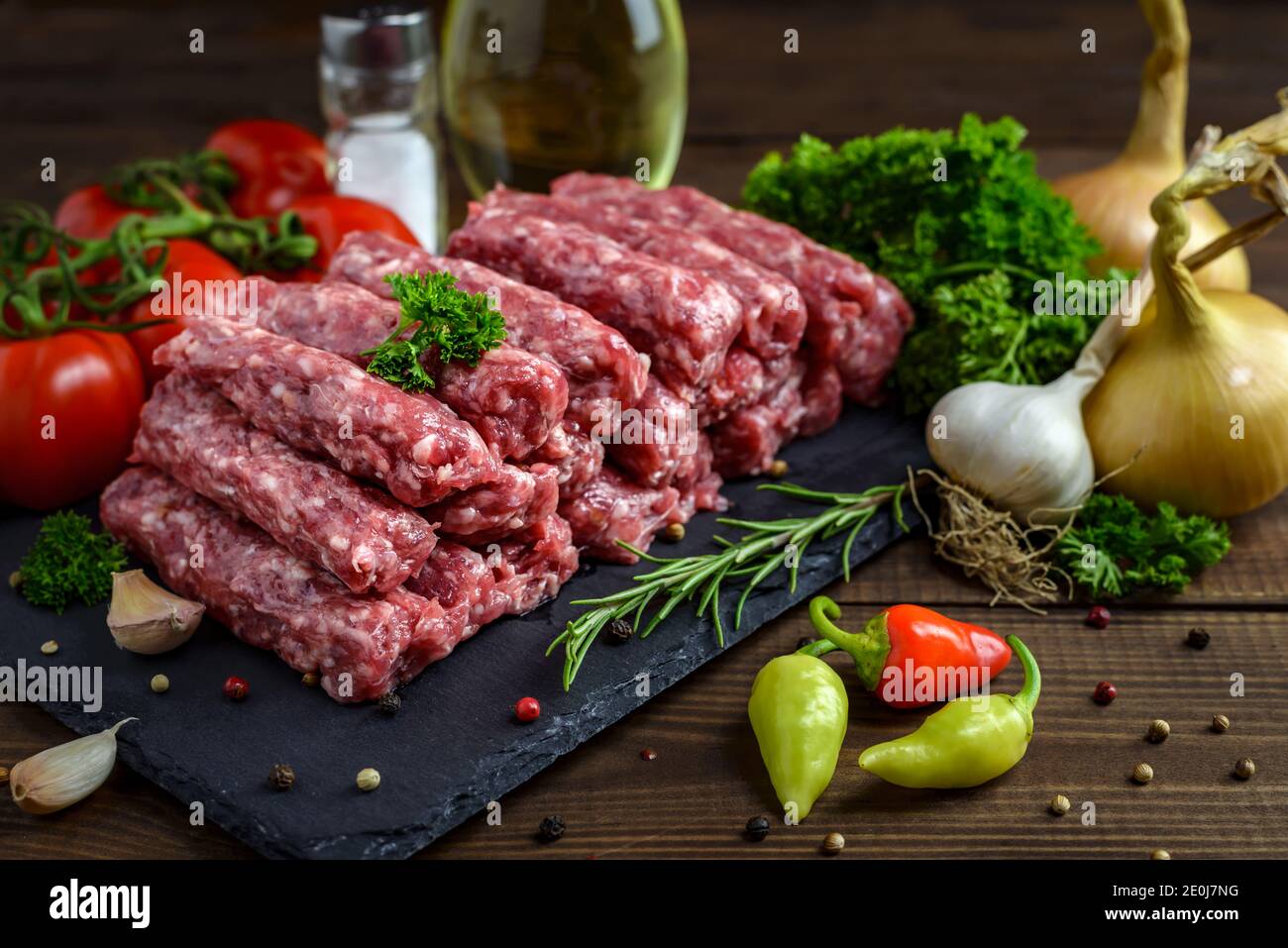 Raw minced meat cevapi ready for barbeque with various fresh vegetables on a wooden table. Selective focus. Stock Photo
