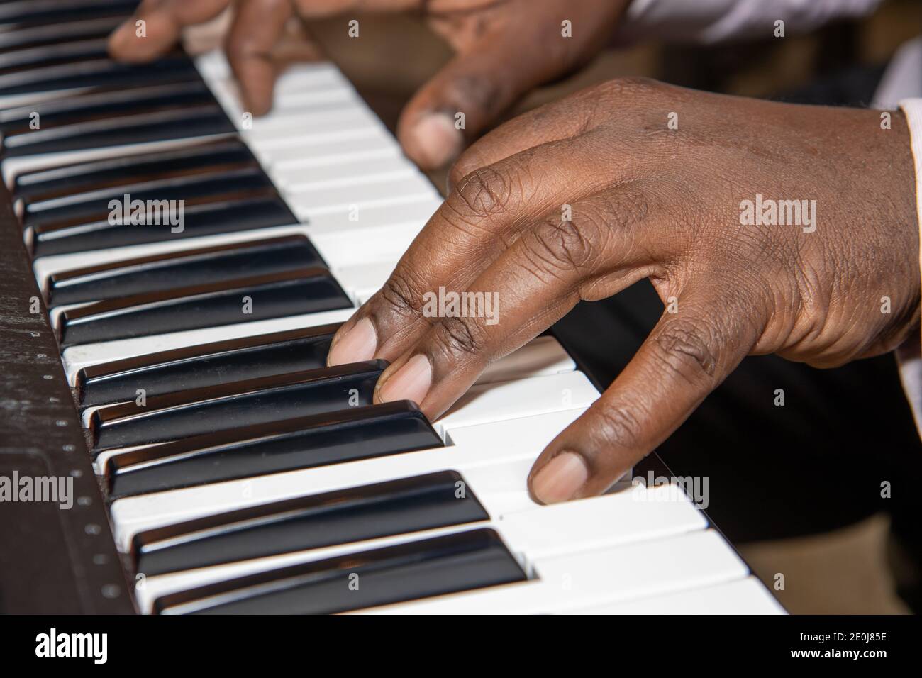 Fingers of an old African American man playing a keyboard piano wearing