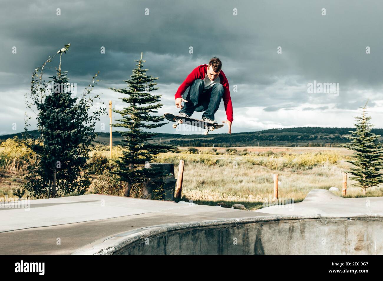 Male skateboarder flipping skateboard in the air at a skatepark Stock Photo