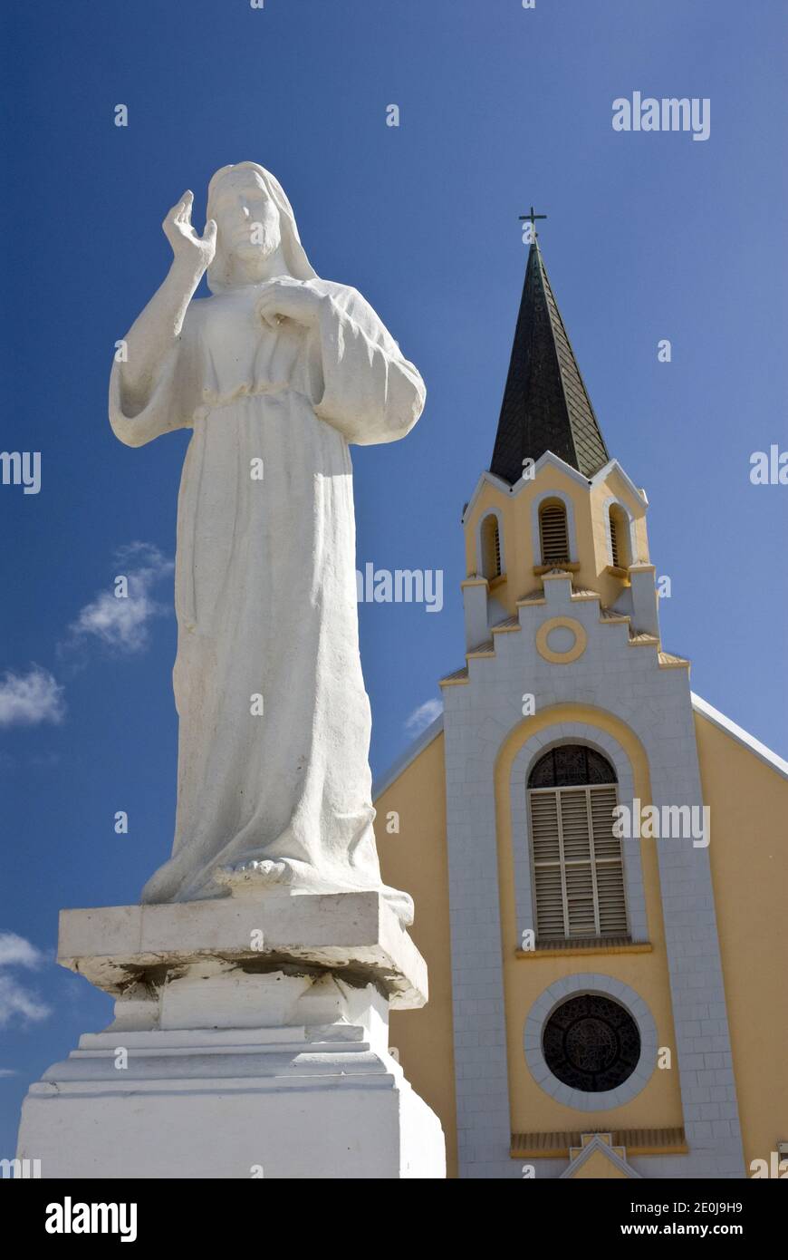 A statue of Jesus stands in front of the historic and colorful St. Anna's Catholic Church, Noord, Aruba. Stock Photo