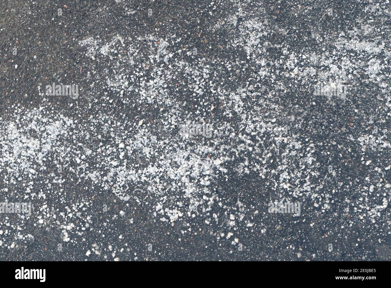 De-icing chemicals reagent on asphalt road. Pavement is sprinkled with technical salt will make the road safe, top view. Stock Photo