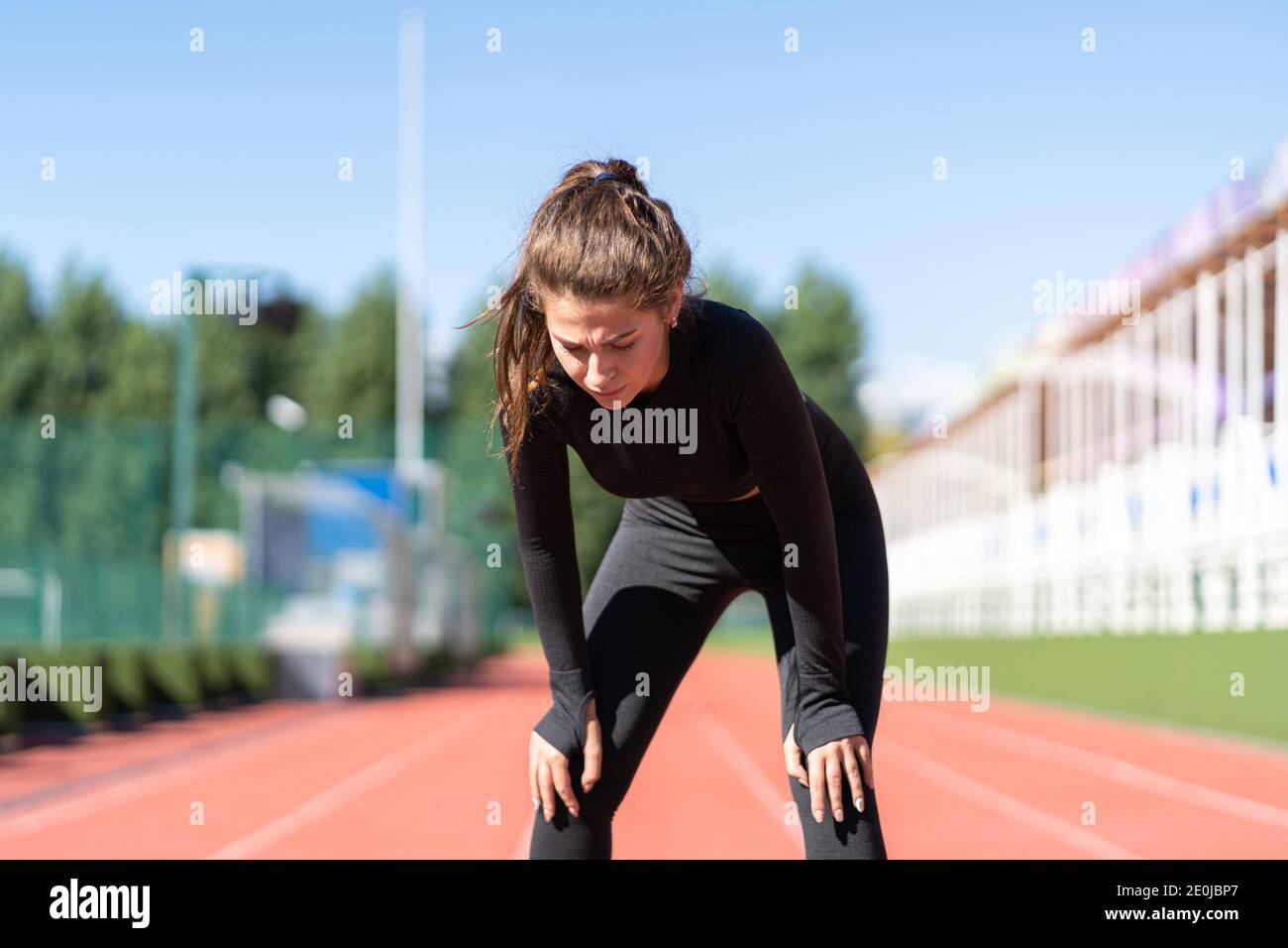 Tired sporty fitness woman in sportswear exhausted breathing after running on a treadmill rubber stadium, taking a break during training, outdoors Stock Photo