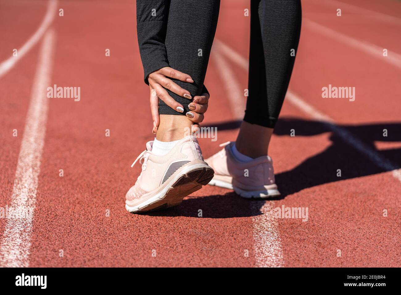 Close up of athletic woman runner touching foot in pain due to sprained ankle, rear view