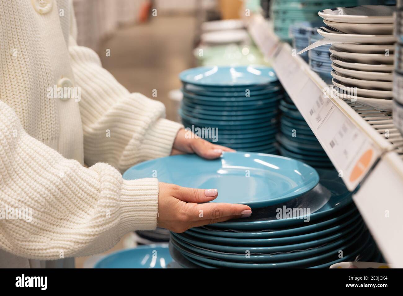 Woman customer choosing and buying blue clay dishes plates, dinner utensil for her kitchen in houseware store or supermarket. Shopping concept. Stock Photo
