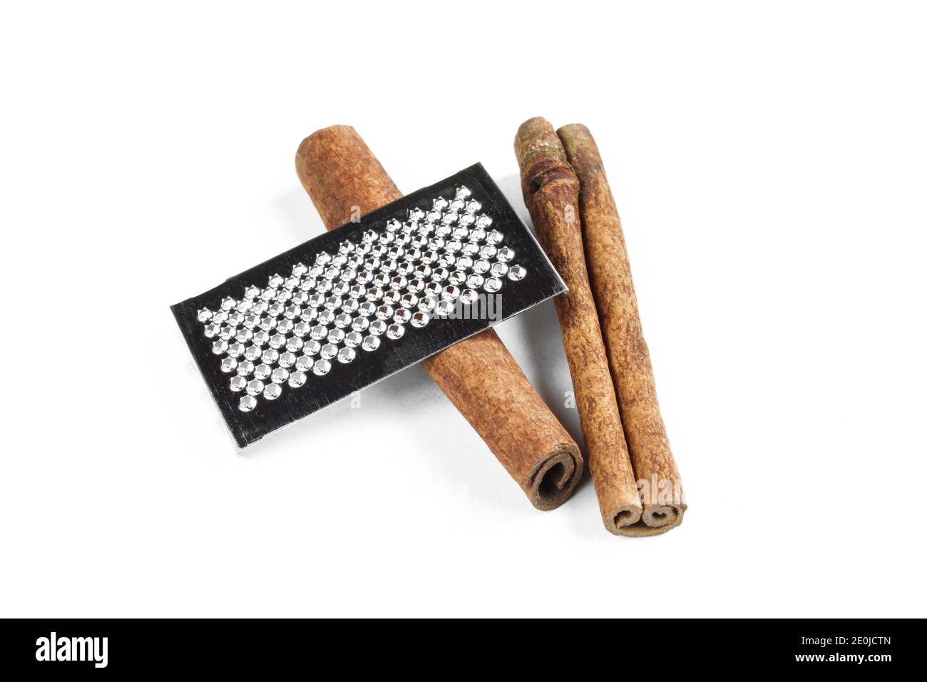 Two brown cinnamon sticks along with metallic grater isolated on white background Stock Photo