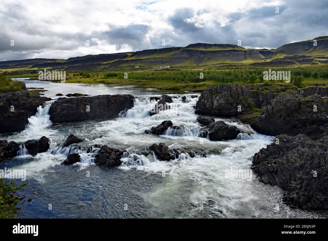 Glanni Waterfall on the Norðurá River in Western Iceland.  Water flows over the black lava rock and mountains rise from the river banks. Stock Photo
