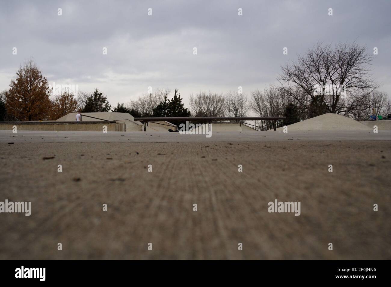 A wide ground-level shot of a rail at a skate park on a cloudy day. Concrete ramps slope in the background. Stock Photo