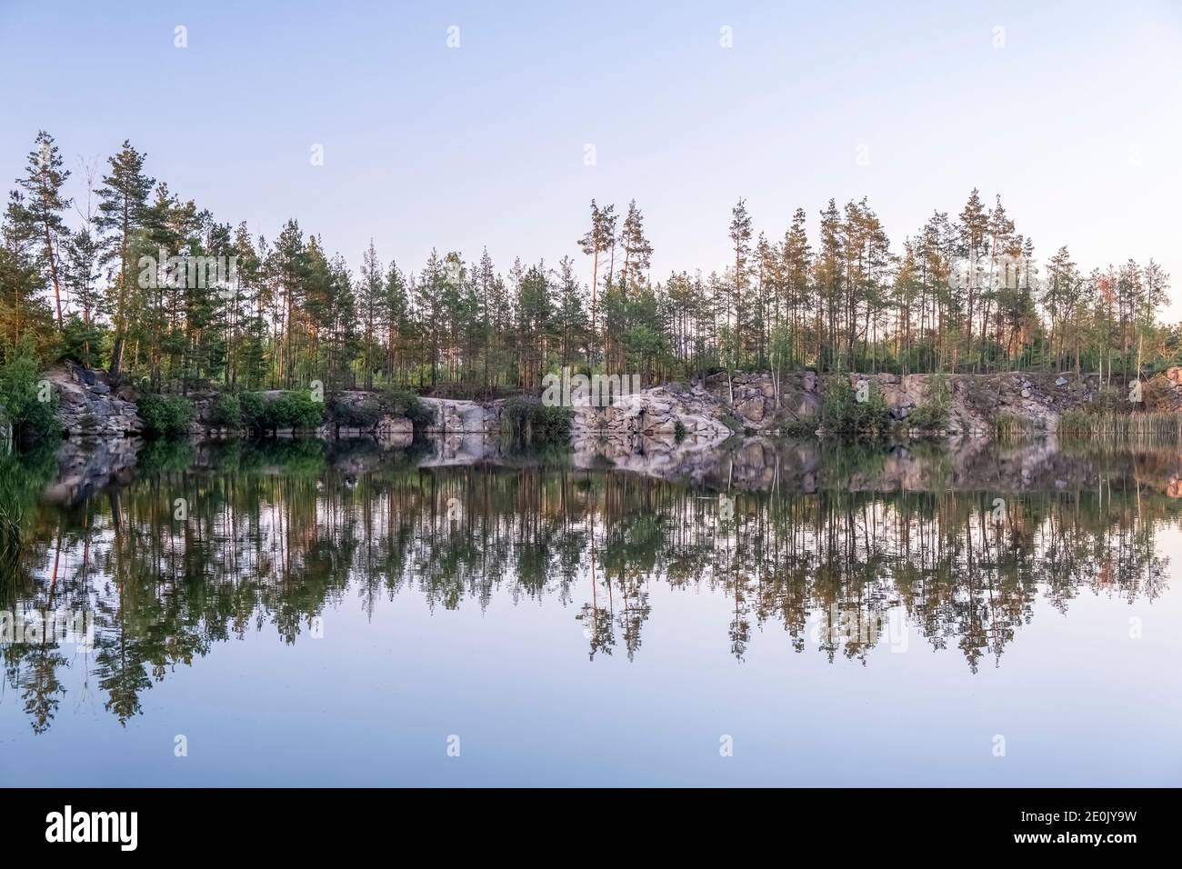 Panoramic view of a beautiful clear lake among granite rocks and a pine forest reflected in the water at sunset in the summer, sun rays shining throug Stock Photo