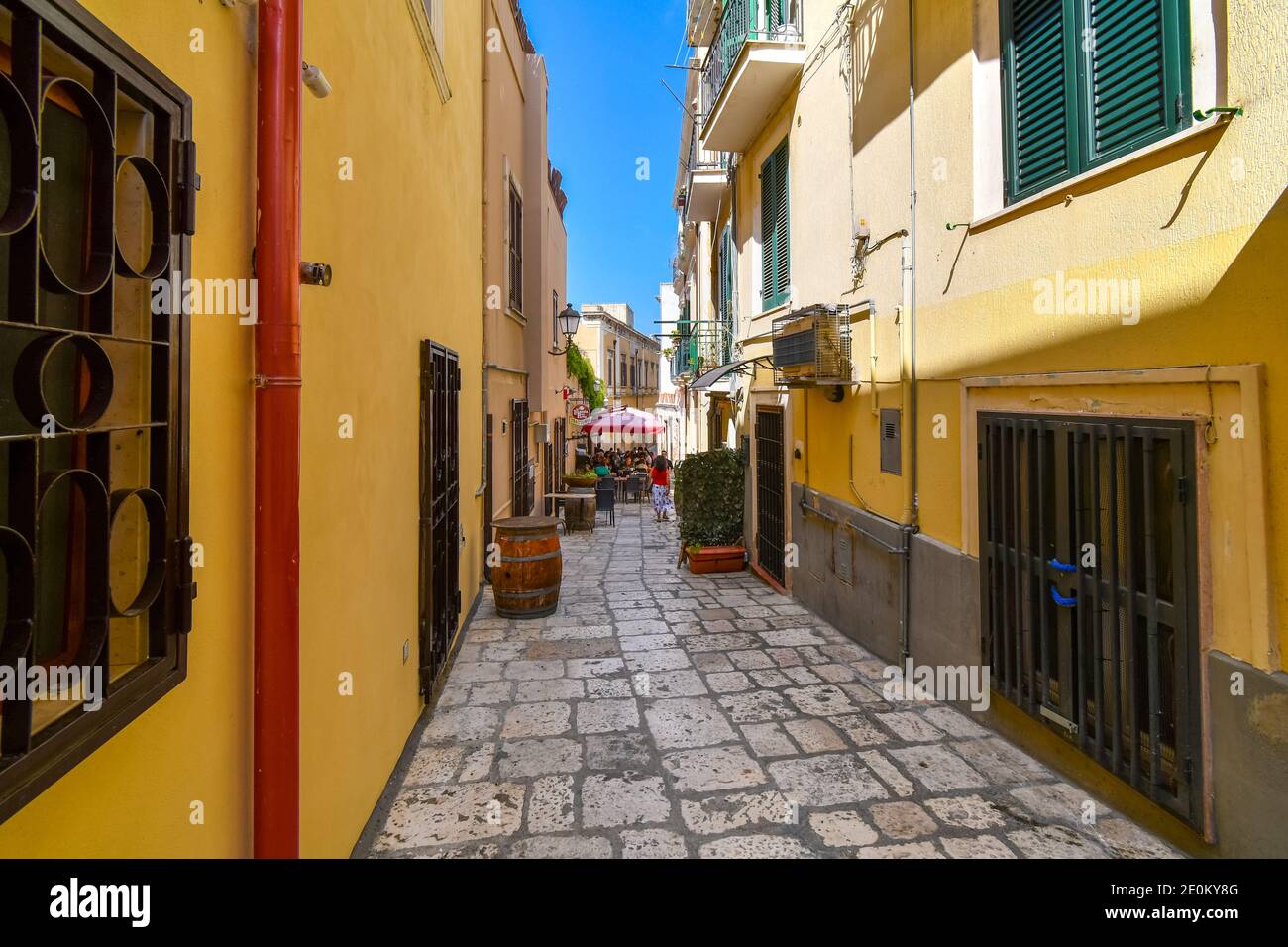 A woman walks down a colorful narrow alley towards a cafe in the Italian city of Brindisi Italy, in the Puglia region. Stock Photo