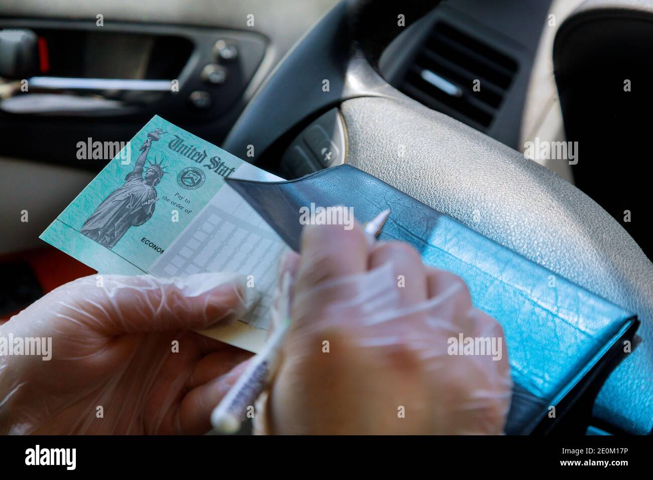 Writing a paper slip depositing government stimulus check with gloves on for safety in car soft focus Stock Photo