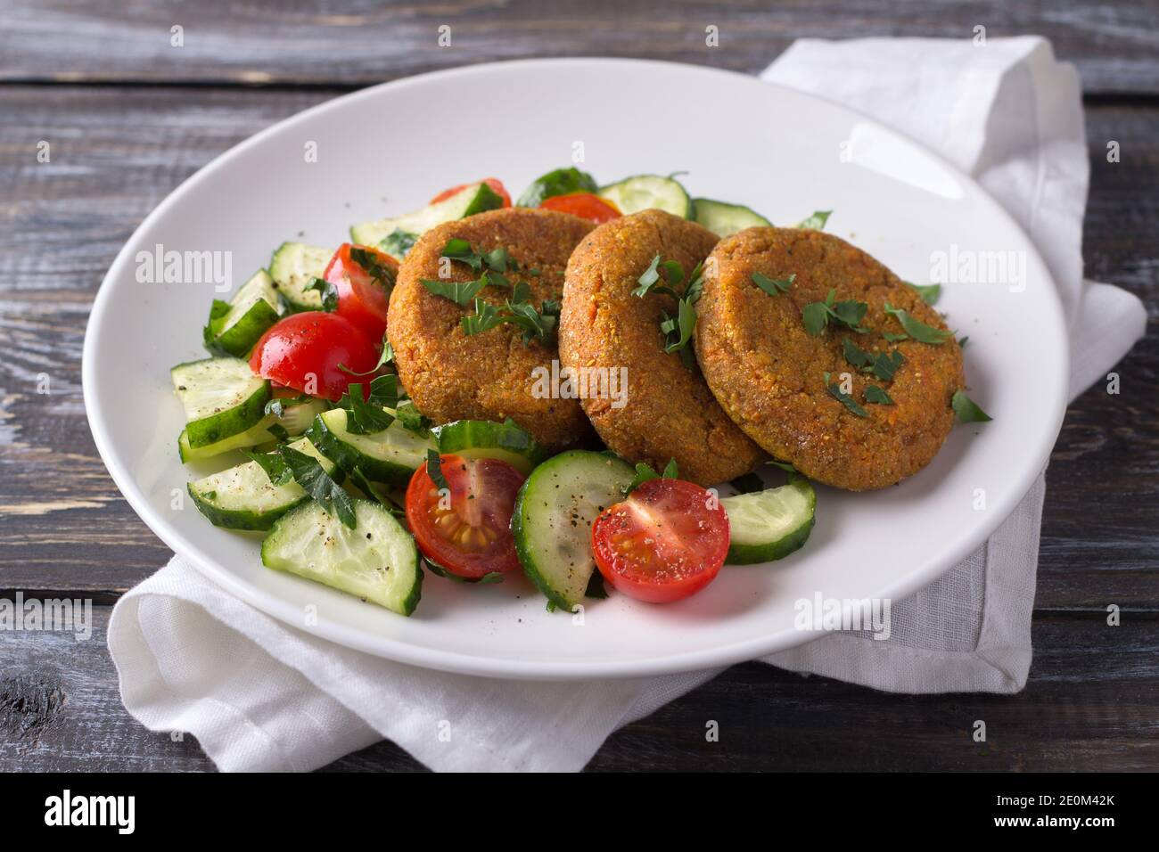 Carrot cutlets with amaranth, salad of fresh cucumbers and tomatoes on a wooden table. Delicious healthy homemade food Stock Photo