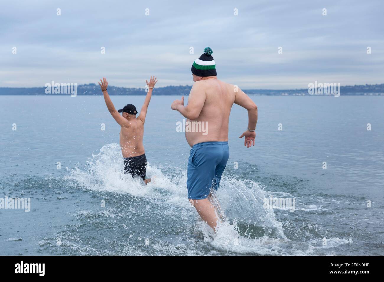 Seattle, Washington, USA. 1st January, 2021. Friends Jimmy Yap and Louis Ibarra run into the frigid waters of Puget Sound at the annual West Seattle Polar Bear Swim at Alki Beach Park. Organizers arranged physically distanced sites and staggered timing along Alki Beach for participants amid a recent moderation of COVID-19 cases in the city. Credit: Paul Christian Gordon/Alamy Live News Stock Photo