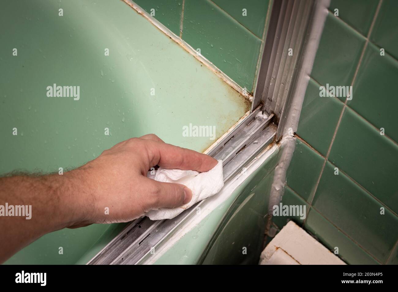 Hand wipes sliding shower door track with towel, in retro colored and styled home bathroom setting. Stock Photo