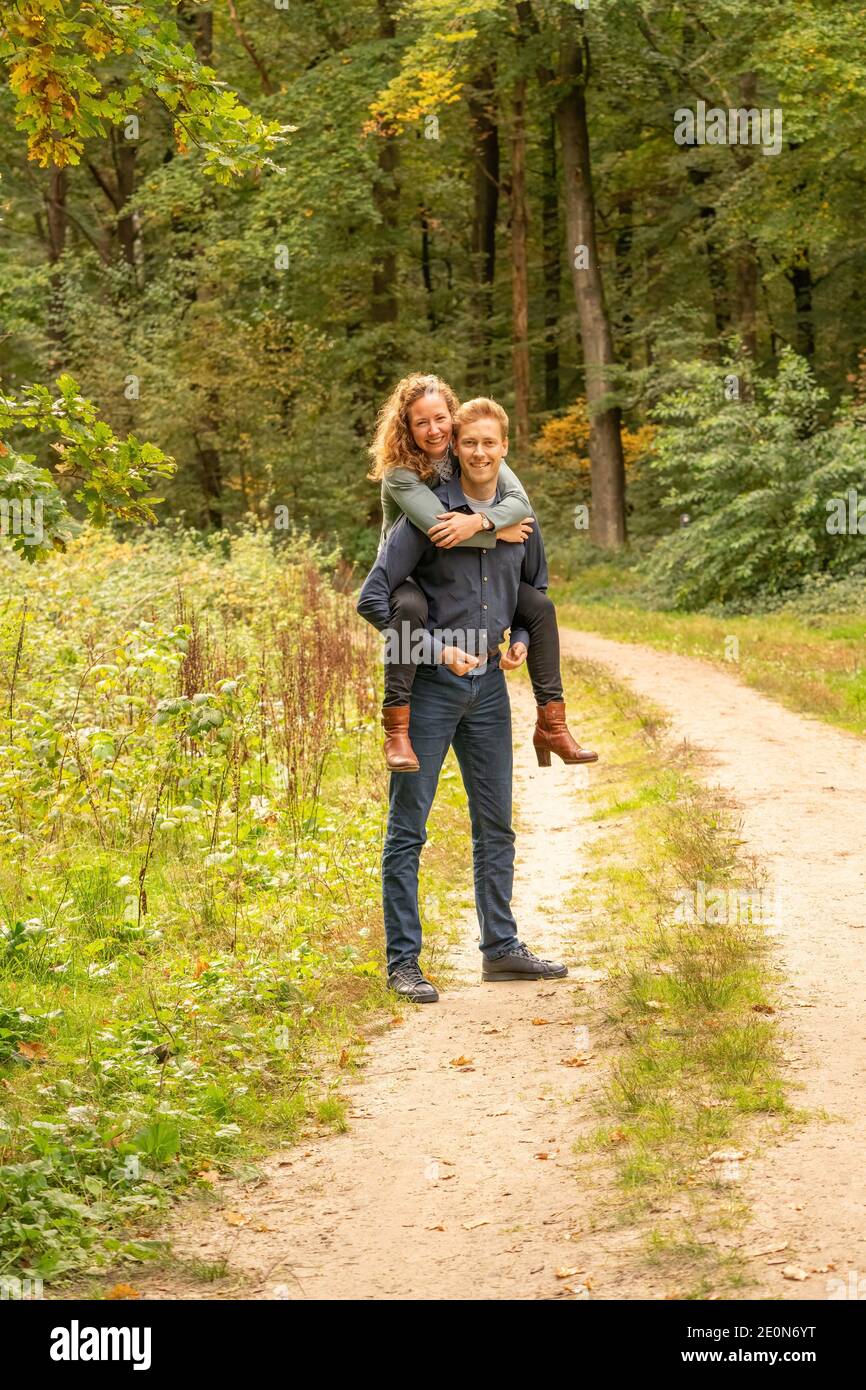 Attractive young couple, man carries woman on his back in the woods. They  stand still on a sandy forest path Stock Photo - Alamy