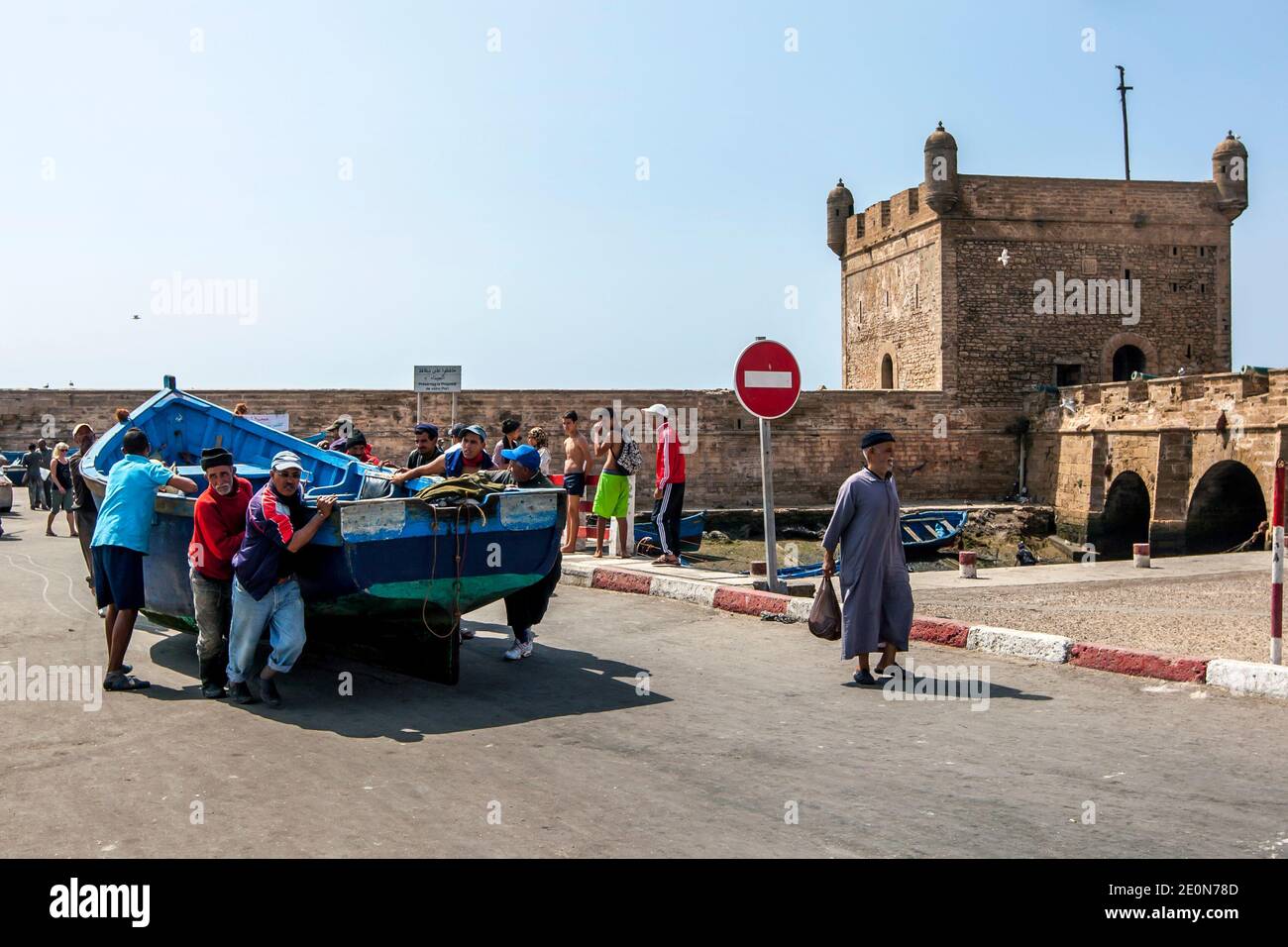 Fishermen use brute force to move a boat along the dock at the fishing port of Essaouira on the Atlantic Ocean of Morocco. Stock Photo