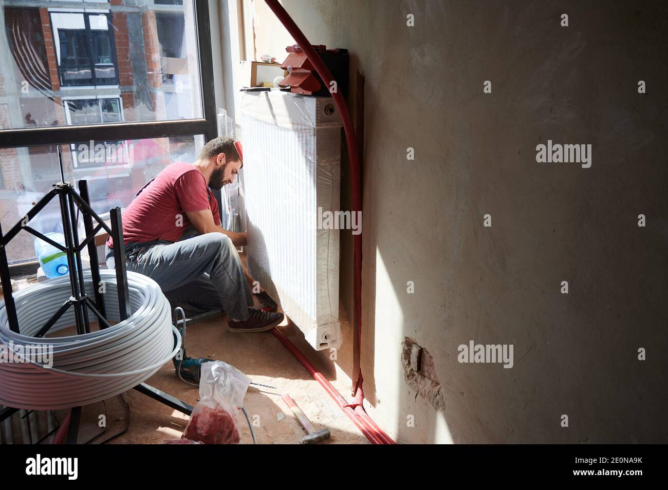 Young plumber connecting water radiator to heating system in new ...