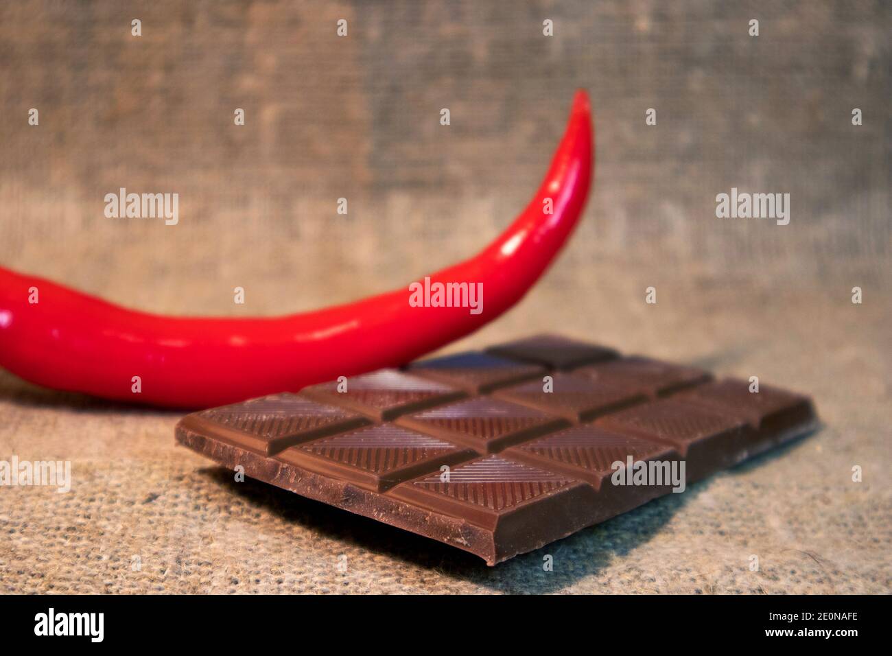 Red hot chilli pepper and broken chocolate bar against rough burlap Stock Photo