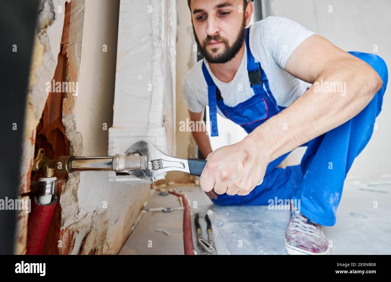 Horizontal snapshot of handsome plumber screwing plumbing fittings with wrench. Close-up of strong arm working with a tool during installation works in new apartment. Focus on hand with instrument. Stock Photo