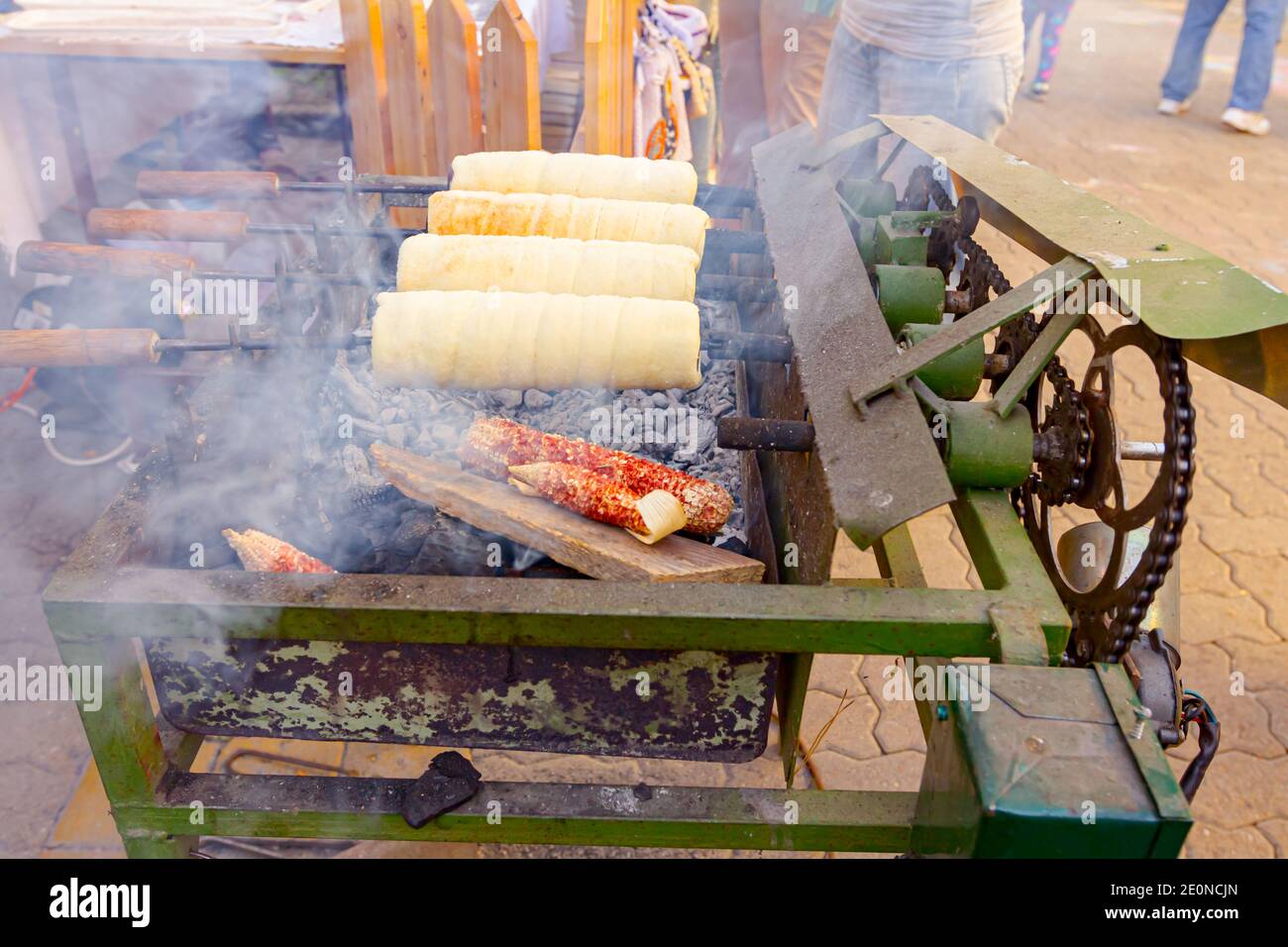 Traditional Hungarian spit cinnamon, chimney cake is rotate for equal baking over glowing charcoal embers at outdoors cooking. Stock Photo